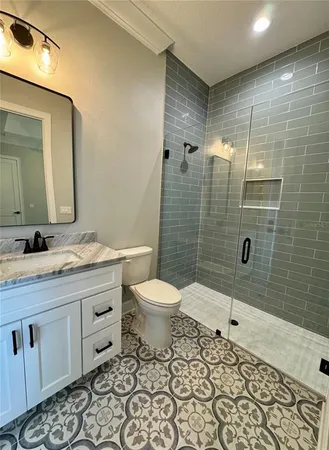 a bathroom with a granite countertop toilet a sink a mirror a shower a window