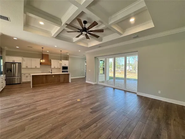 an empty room with wooden floor kitchen view and windows