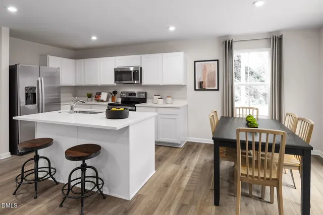 a kitchen with stainless steel appliances granite countertop a dining table chairs refrigerator and sink