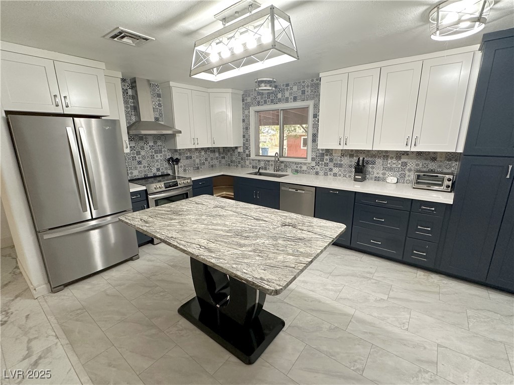 2025 Whipple Avenue Logandale, NV 89021 - Photo 15 of 44 Kitchen with quartz counters, stainless steel appliances, white cabinetry, wall chimney range hood, tasteful backsplash, and a textured ceiling