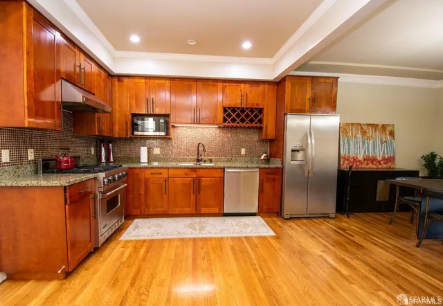 a large kitchen with stainless steel appliances granite countertop a stove a sink dishwasher a refrigerator and wooden cabinets with wooden floor