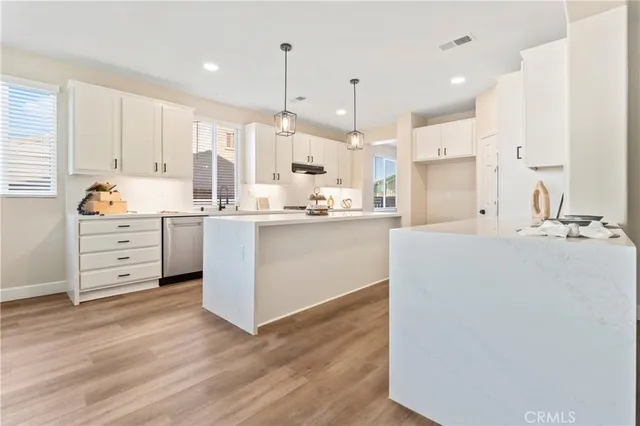 a room with stainless steel appliances kitchen island granite countertop a sink a cabinets and wooden floor