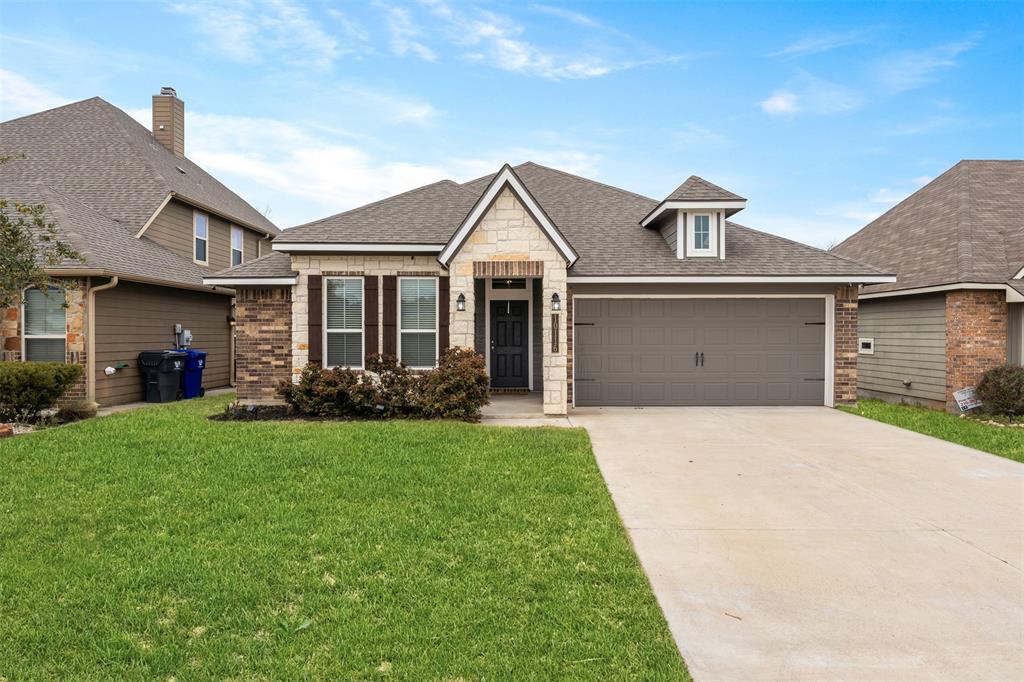 View of front of home featuring an attached garage, a front yard, roof with shingles, and stone siding