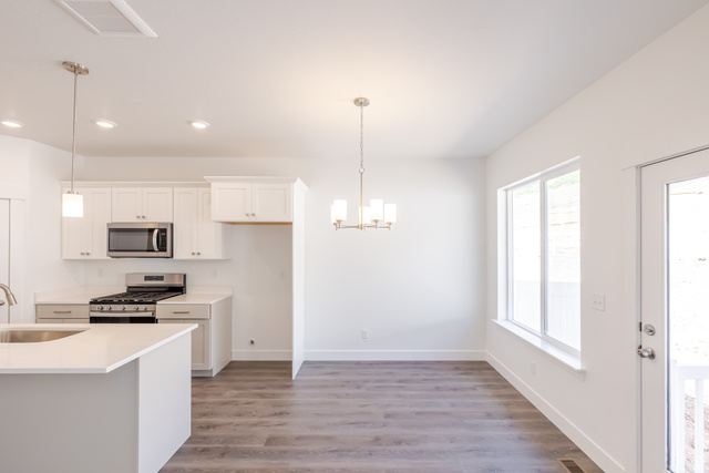 5287 South Acacia Drive, Unit 714 Mapleton, UT 84664 - Photo 7 of 21 Open-concept kitchen and dining area featuring wood-finish flooring, white cabinetry, a kitchen island with sink, stainless steel appliances, and abundant natural light from a large window and glass-paneled door