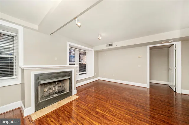a view of an empty room with wooden floor fireplace and a window