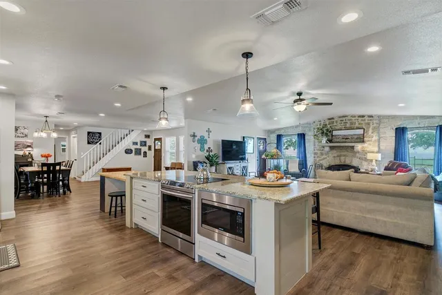 a view of a kitchen with kitchen island a stove a sink a dining table and chairs with wooden floor
