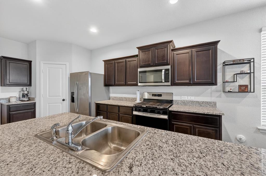9604 Cherryville Road Fort Worth, TX 76108 - Photo 15 of 40 Kitchen featuring an island with a stainless steel double basin sink, granite countertops, dark wood cabinetry, and stainless steel appliances