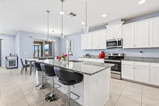 a kitchen with stainless steel appliances granite countertop a sink a stove a refrigerator cabinets and chairs