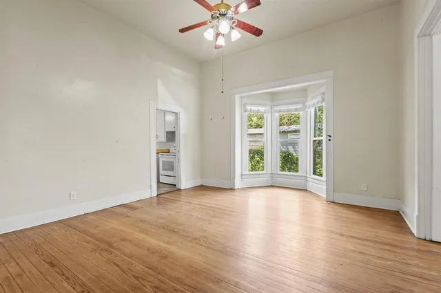 an empty room with wooden floor chandelier and windows