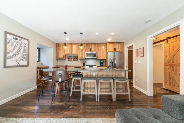 a kitchen with stainless steel appliances granite countertop a stove top oven a refrigerator a dining table and chairs with wooden floor