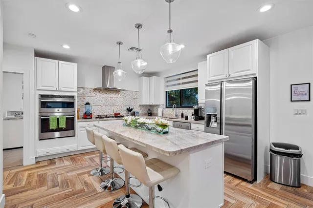 a kitchen with stainless steel appliances granite countertop a refrigerator a sink dishwasher a stove and white cabinets with wooden floor