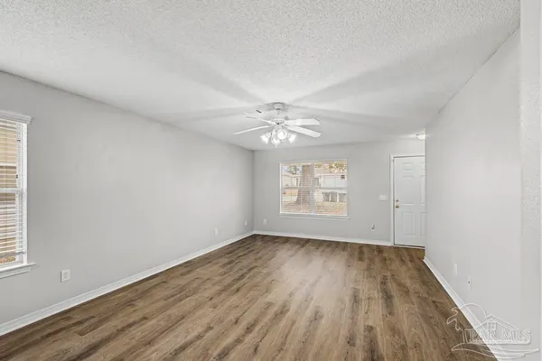 an empty room with wooden floor chandelier fan and windows