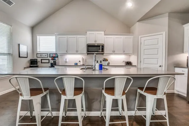 a white kitchen with granite countertop a dining table chairs and a refrigerator