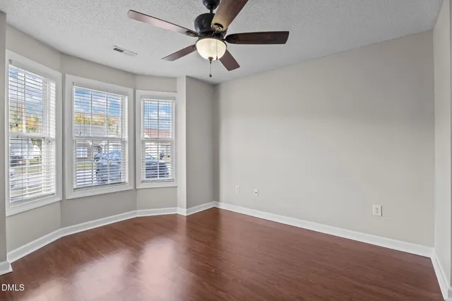 an empty room with wooden floor fan and windows