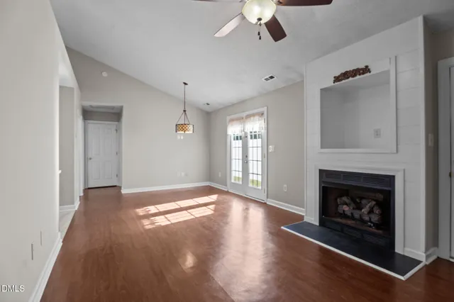 a view of an empty room with wooden floor fireplace and a window