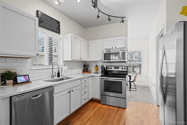 a kitchen with stainless steel appliances granite countertop a refrigerator a sink dishwasher a stove and white cabinets with wooden floor