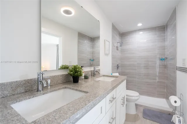 a bathroom with a granite countertop sink a toilet a mirror and shower