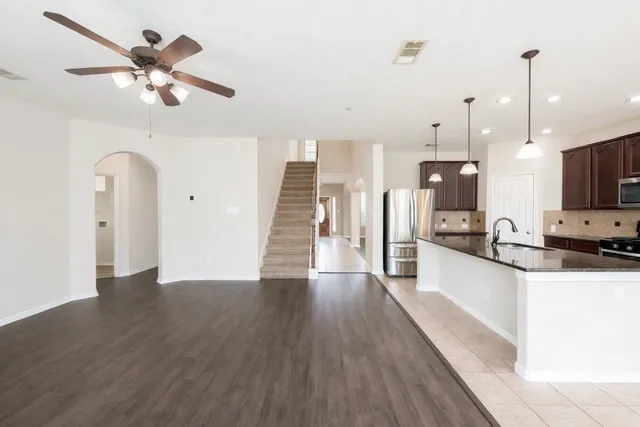 a kitchen with stainless steel appliances kitchen island granite countertop a refrigerator a stove and a sink with wooden floor