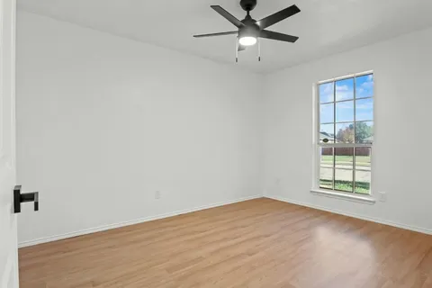 an empty room with wooden floor fan and windows