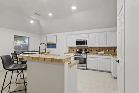 a kitchen with stainless steel appliances granite countertop a stove top oven a sink a refrigerator and white cabinets