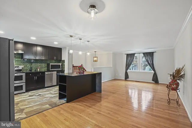 a living room with stainless steel appliances kitchen island granite countertop a refrigerator a stove and a sink with wooden floor