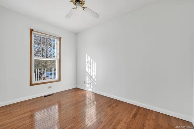 an empty room with wooden floor chandelier fan and windows