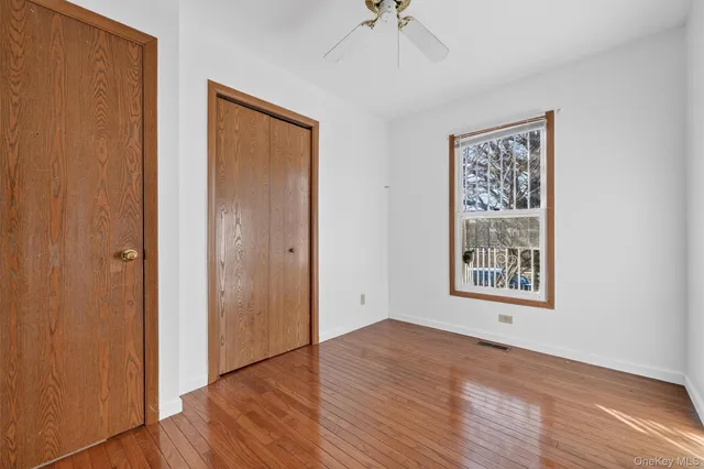 an empty room with wooden floor chandelier fan and windows
