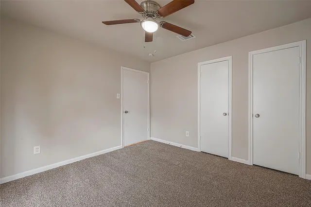 an empty room with chandelier fan and windows