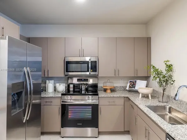 a kitchen with stainless steel appliances granite countertop a sink a stove a refrigerator and a white cabinets