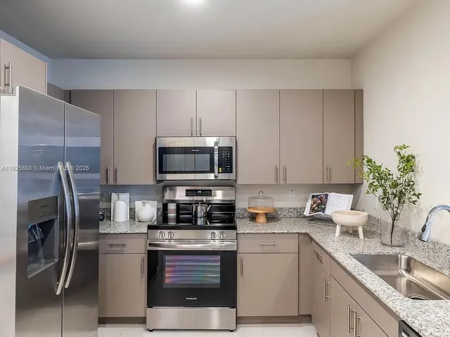 a kitchen with stainless steel appliances granite countertop a sink a stove a refrigerator and a white cabinets