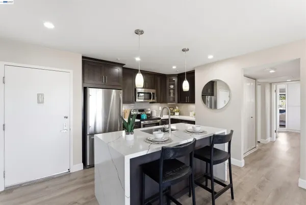 a kitchen with stainless steel appliances kitchen island granite countertop a refrigerator a sink a stove a dining table and chairs with wooden floor