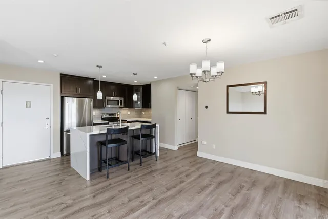 a kitchen with stainless steel appliances a stove top oven a refrigerator a dining table and chairs with wooden floor