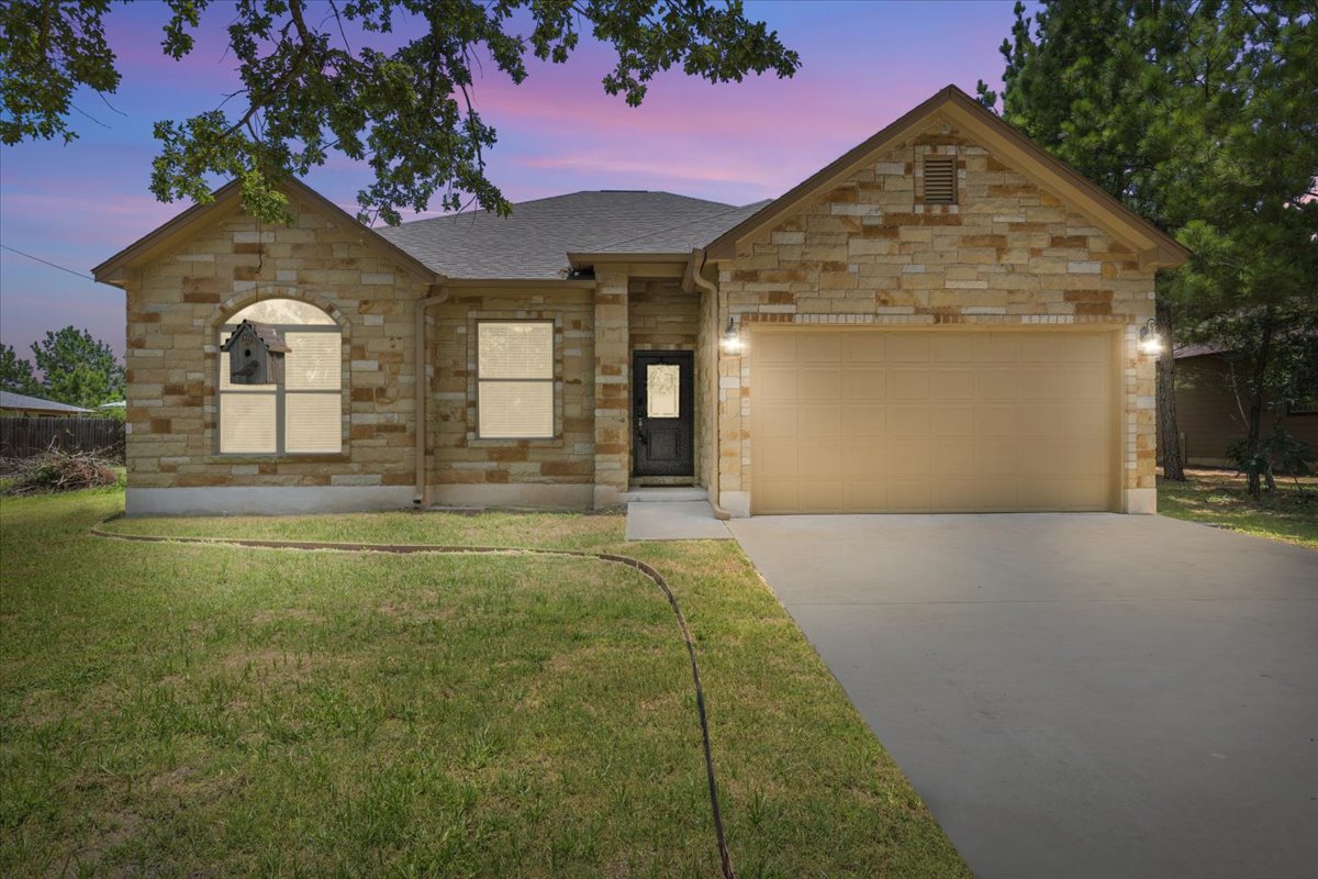 145 Cardinal Loop Paige, TX 78659 - Photo 3 of 40 Crafted with warm stone and an inviting driveway, this home presents a welcoming facade.