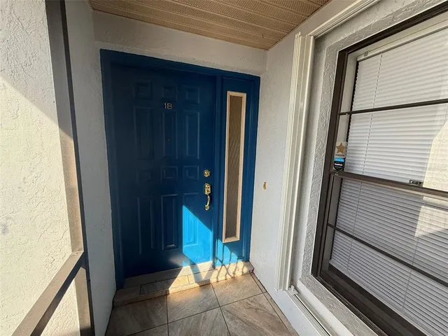 an empty room with chandelier fan and kitchen view