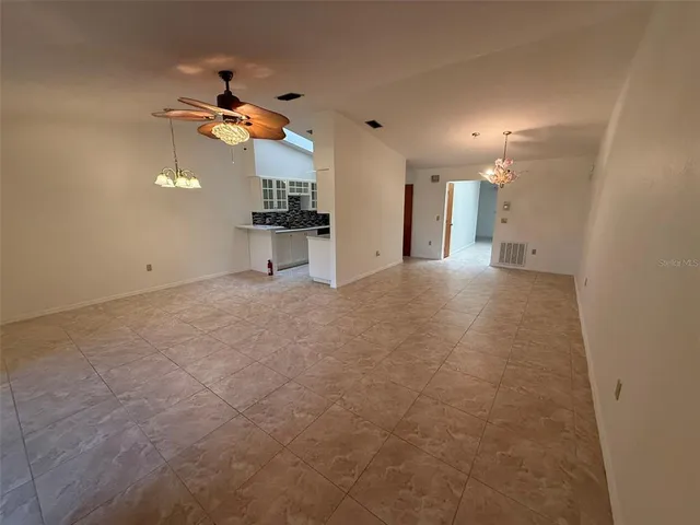 an empty room with chandelier fan and windows