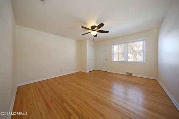 a view of empty room with wooden floor and fan