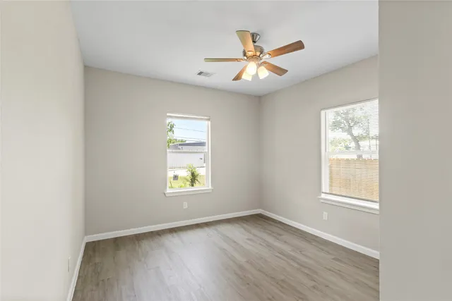 an empty room with wooden floor window and ceiling fan