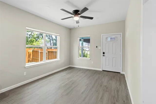 an empty room with wooden floor chandelier fan and windows