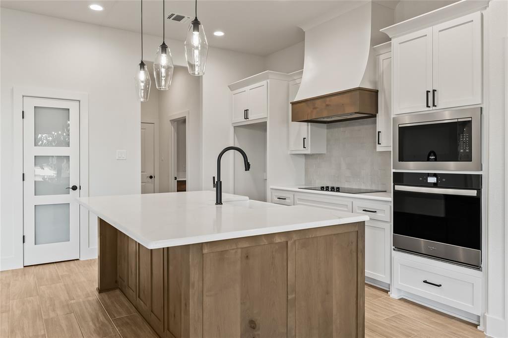 7004 Rnch Vw Place Springtown, TX 76082 - Photo 9 of 25 Kitchen featuring a center island with a white countertop, white cabinetry, integrated stainless steel appliances, a wood-finish range hood, and wood-finish flooring