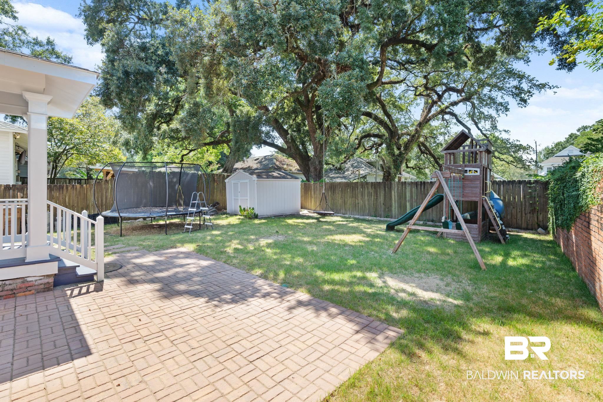 10 South Monterey Street Mobile, AL 36604 - Photo 38 of 45 Fenced backyard with a trampoline, a playground, a patio, and a shed