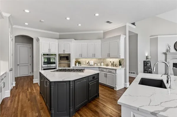 a kitchen with stainless steel appliances kitchen island granite countertop a refrigerator a sink dishwasher and white cabinets with wooden floor