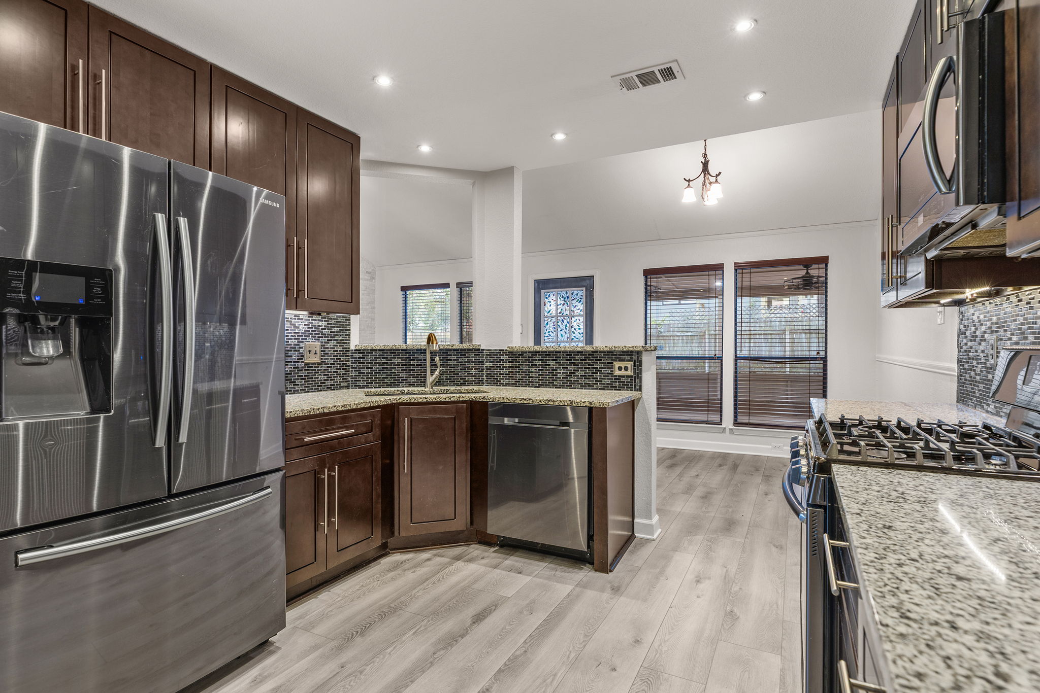 2409 Water Well Lane Austin, TX 78728 - Photo 10 of 22 Contemporary kitchen featuring dark wood cabinetry, stainless steel appliances, a mosaic tile backsplash, light-toned wood-finish flooring, and recessed lighting