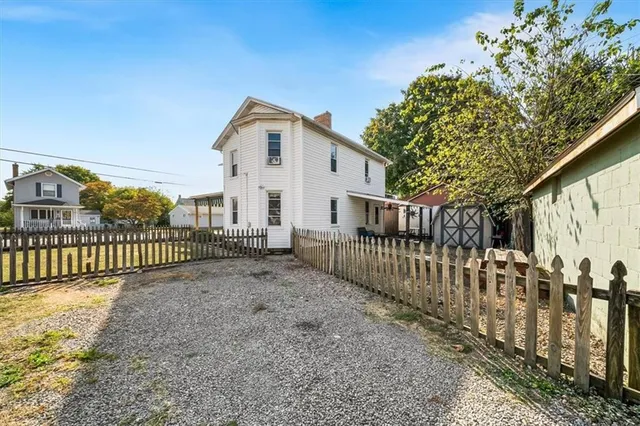 a view of a white house with large trees and wooden fence