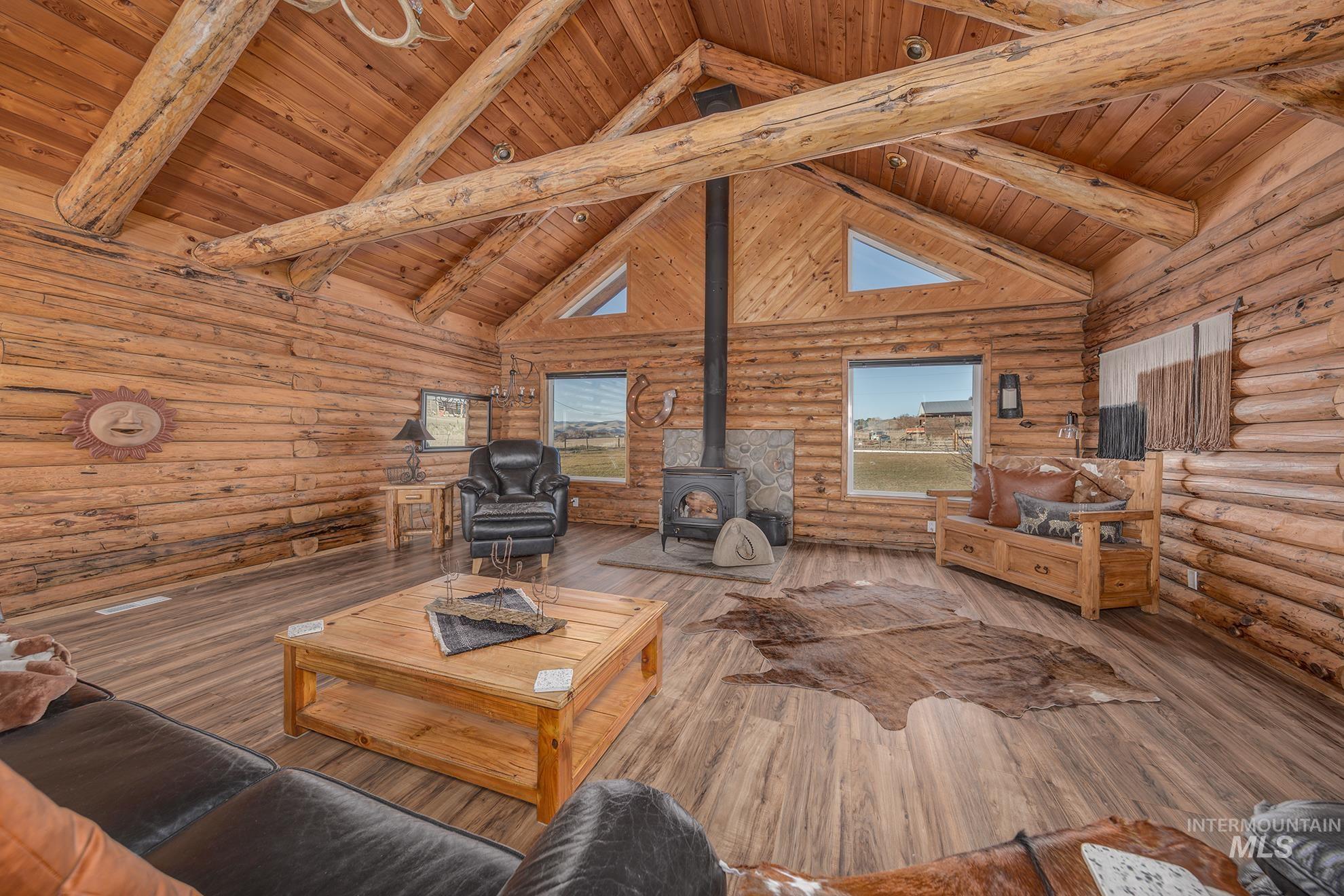 1855 Jones Road Weiser, ID 83672 - Photo 22 of 34 Living area with rustic walls, a wood stove, a high wooden beamed ceiling, and hardwood / wood-style flooring