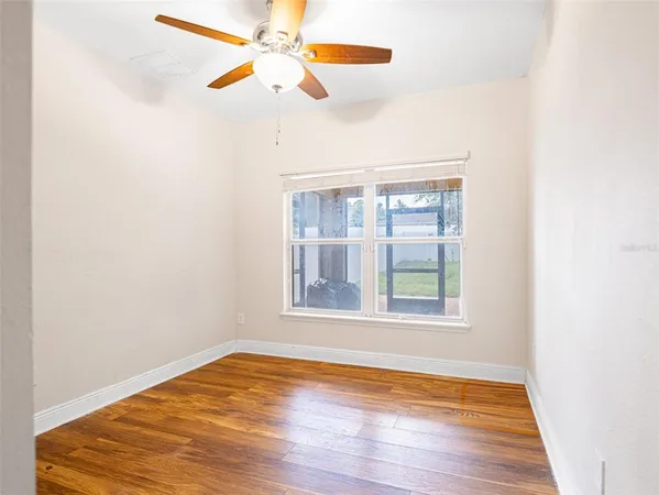an empty room with wooden floor fan and windows