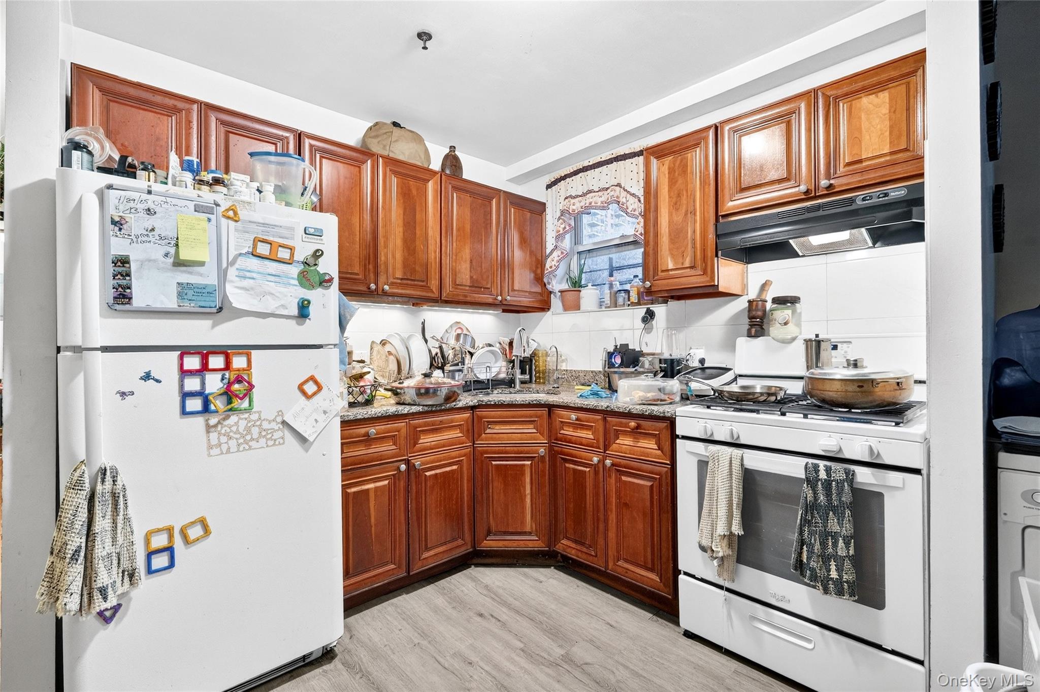 1459 Rosedale Avenue Bronx, NY 10460 - Photo 12 of 37 Kitchen featuring white appliances, tasteful backsplash, under cabinet range hood, dark stone countertops, and brown cabinetry
