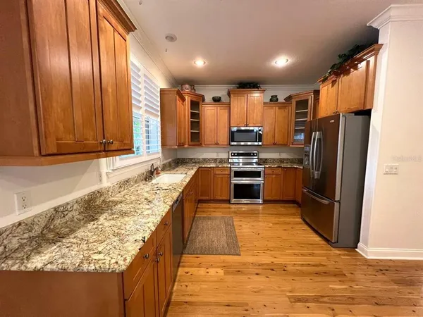 a large kitchen with kitchen island granite countertop wooden cabinets a sink a stove a refrigerator and blue cabinets