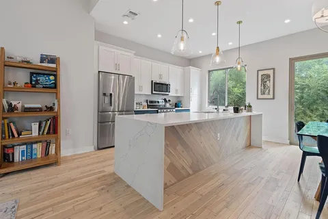 a kitchen with stainless steel appliances granite countertop a refrigerator a stove a microwave and a bookshelf with wooden floors