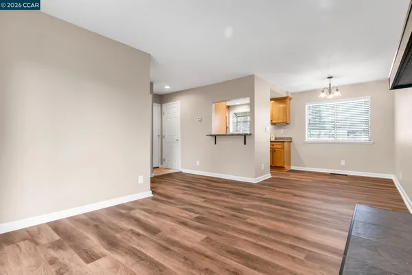 a view of empty room with wooden floor and kitchen view