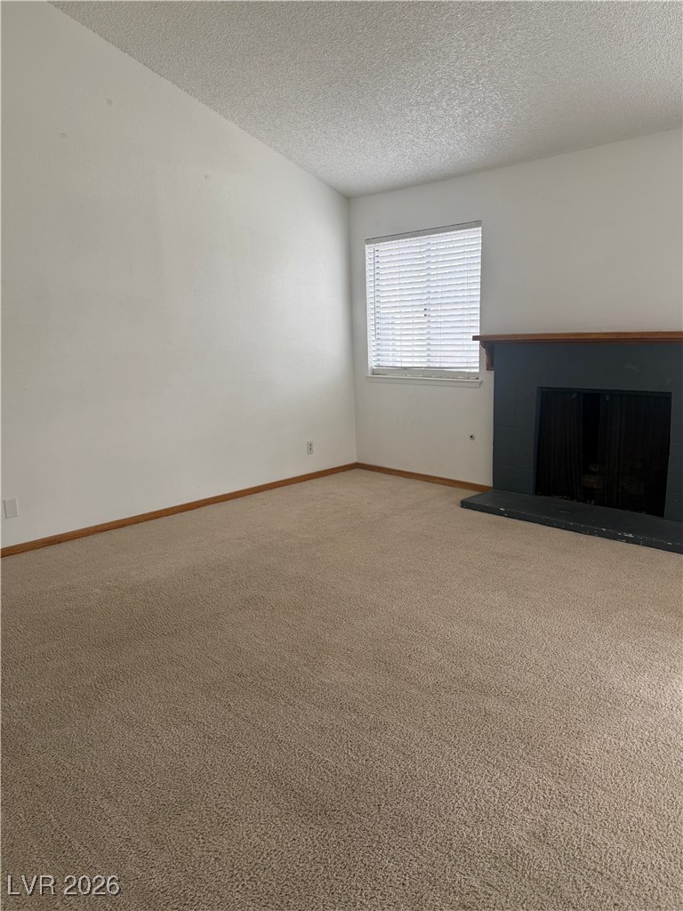 5311 South Sandhill Road Las Vegas, NV 89120 - Photo 14 of 24 Unfurnished living room featuring a fireplace with raised hearth, carpet flooring, and a textured ceiling
